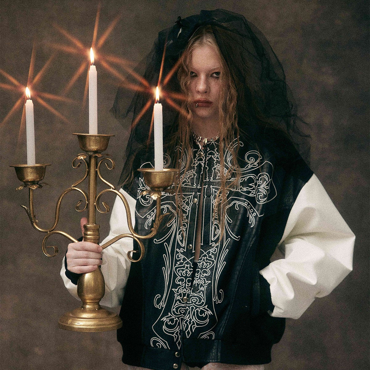 Model holding candle wearing BlackSanctum gothic cross streetwear jacket