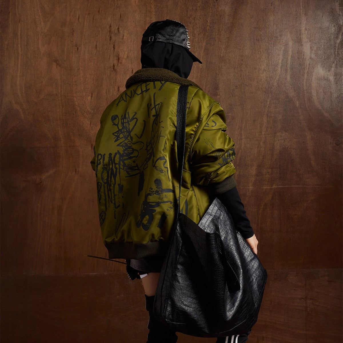 Close up of model wearing olive green graffiti print winter jacket with street style aesthetic and zip front