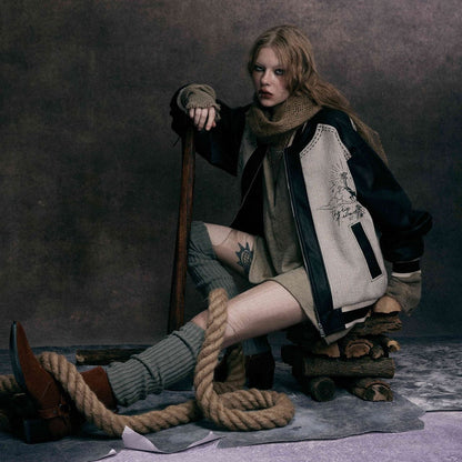 Model sitting wearing MarkedLeather streetwear bomber jacket with contrast leather sleeves and vintage graphic print