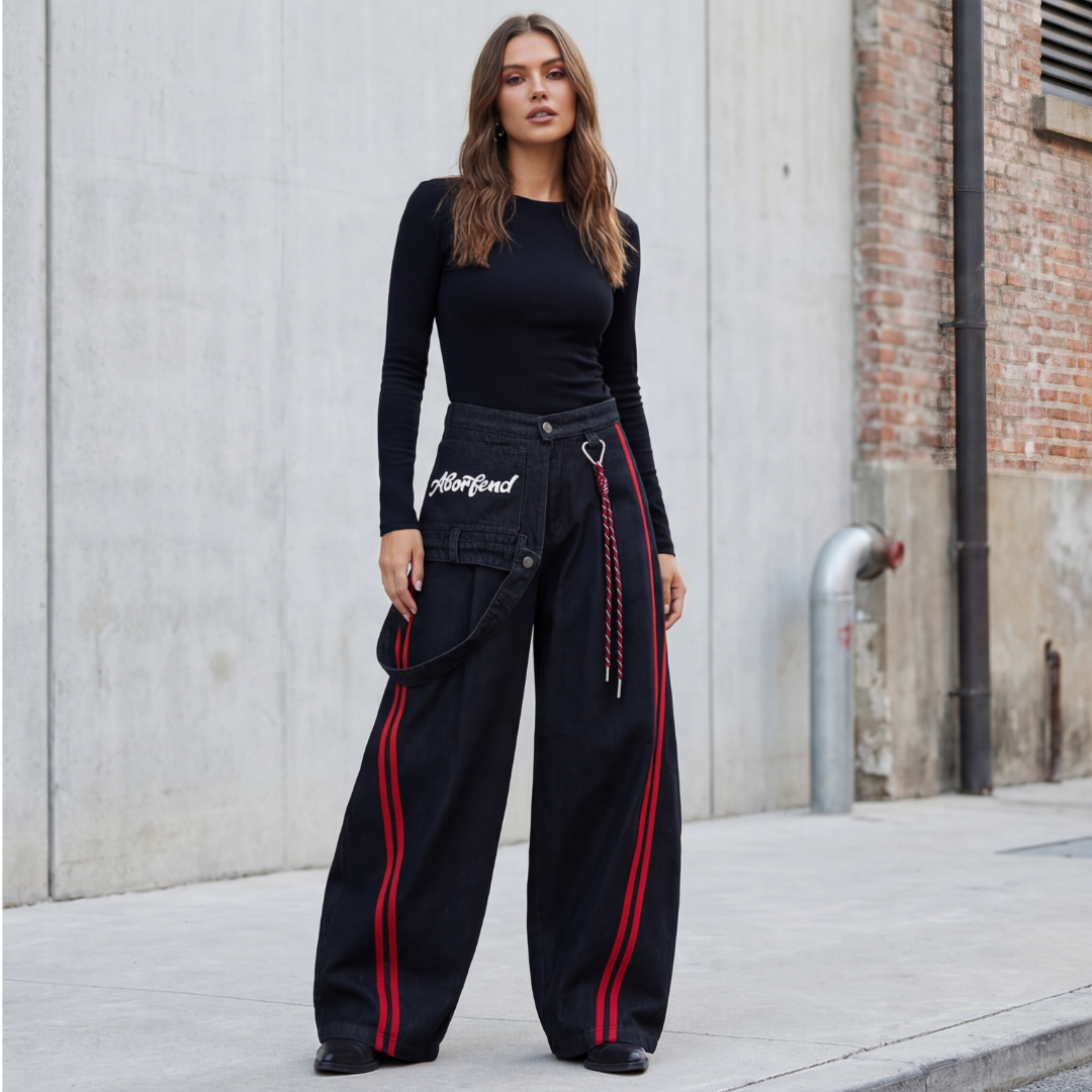 Woman wearing a black outfit with red stripes standing against a concrete wall.